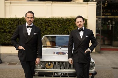Black double-breasted tuxedos with shawl and peak lapels and bow ties, worn by two models by a vintage car