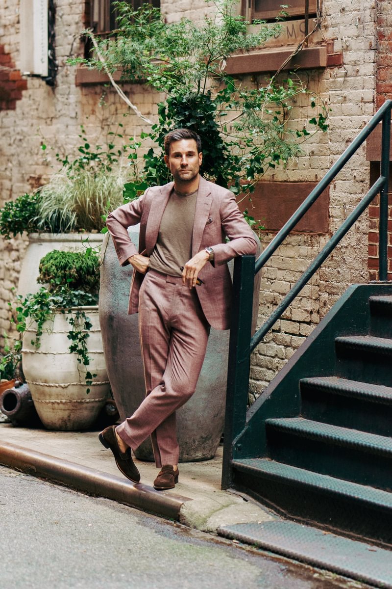 Shane wearing a dusty rose blend suit paired with a taupe crewneck tee and loafers, styled casually by Michael Andrews Bespoke in a garden alley setting - custom suits nyc bespoke tailor midtown, noho