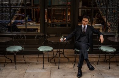 MAB ambassador Austin Pollak seated outside a London café in a midnight green herringbone three-piece suit crafted from Dormeuil Amadeus cloth.