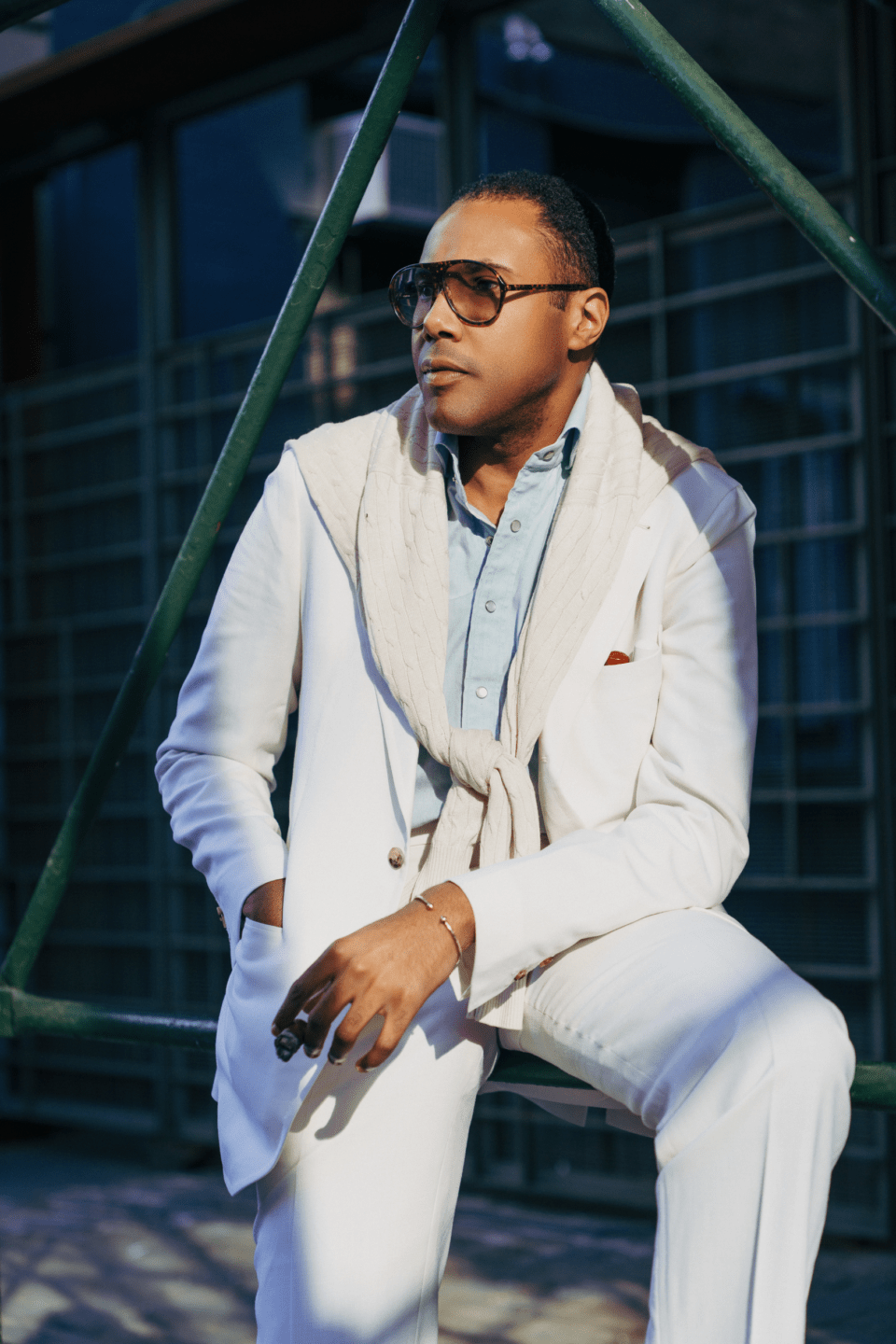 White solid suit styled with a light blue shirt and a cream cable-knit sweater draped over the shoulders