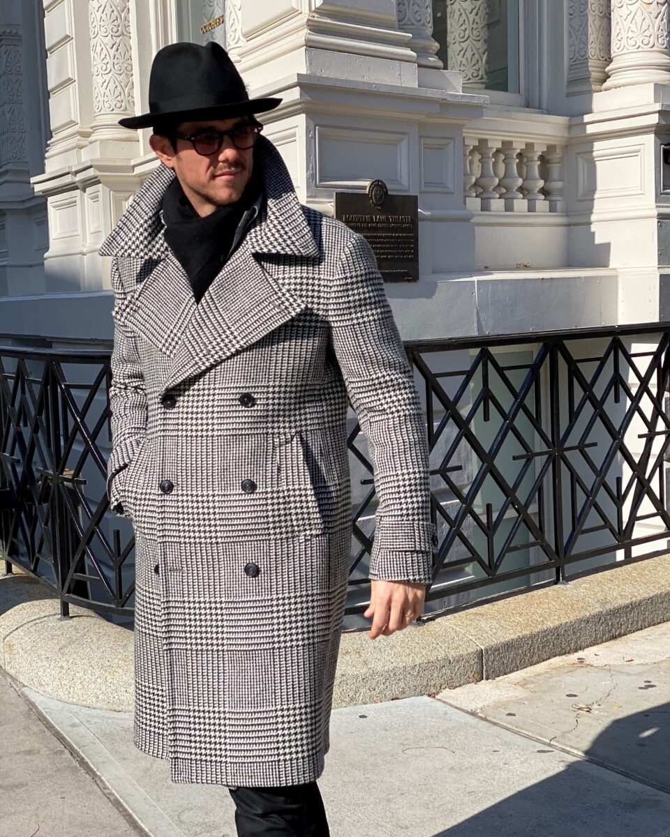 (product) Bespoke Black & White Glen Urquhart Great Coat styled with a black hat outdoors