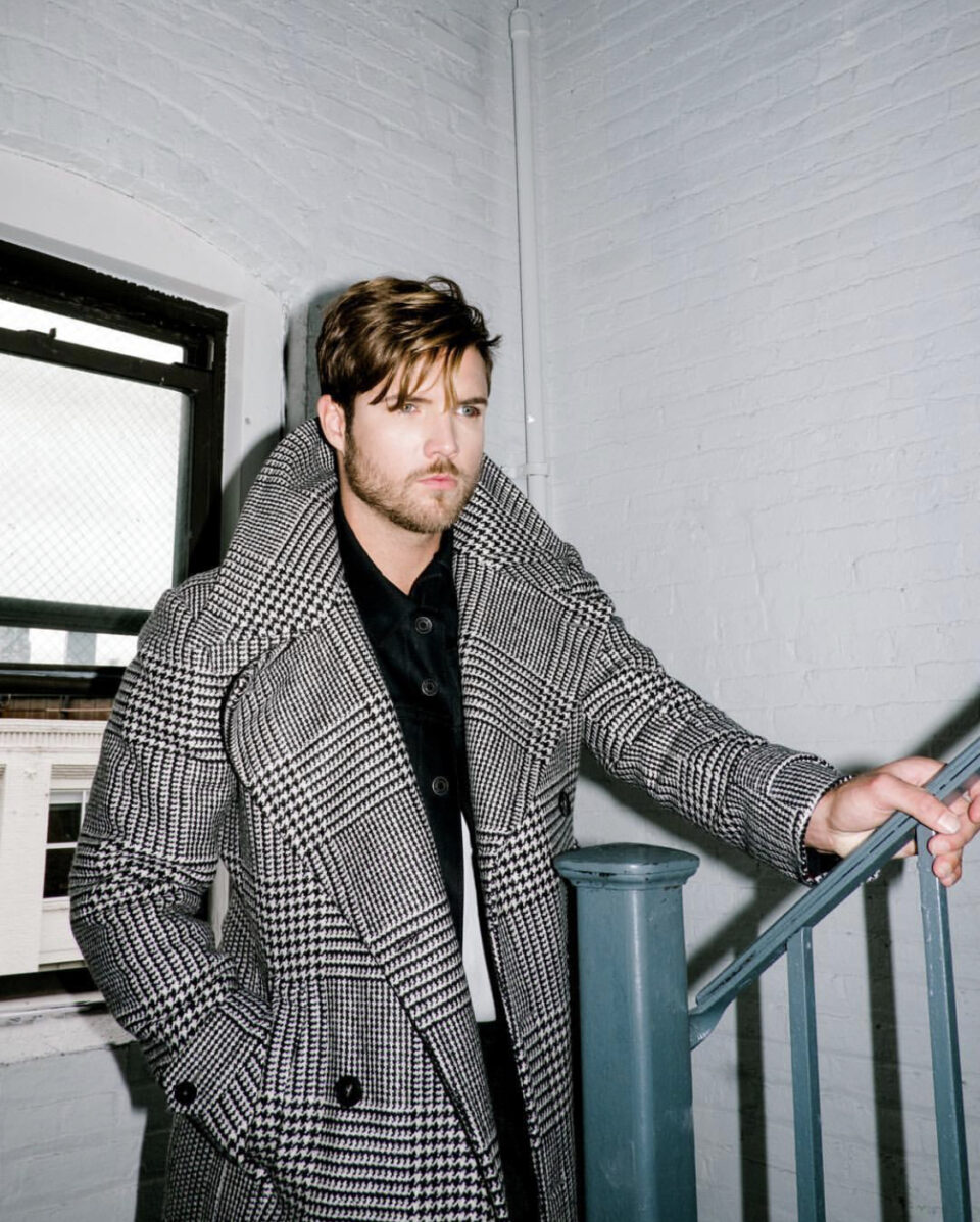 (product) Bespoke Black & White Glen Urquhart Great Coat with a wide collar, styled with a black shirt, indoors