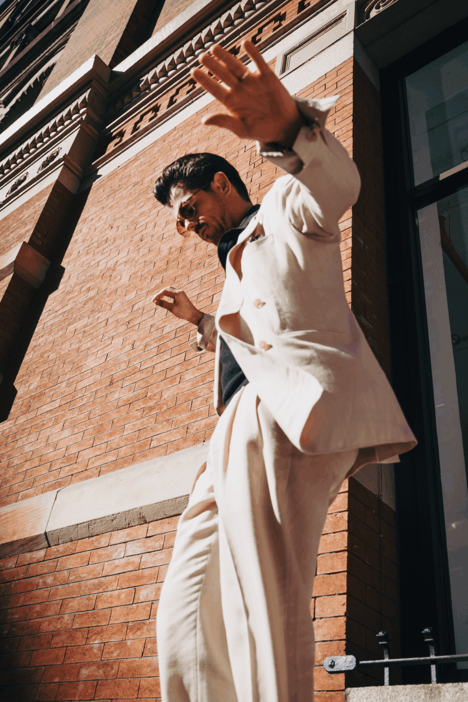 Cory in a beige double-breasted suit with open-collar shirt, caught mid-motion in bright sunlight