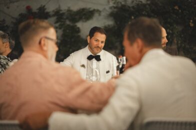 Guests in tailored eveningwear seated around a candlelit dinner table, with Michael in a white tuxedo jacket and black bow tie at the Pitti SS 2024 Arno Dinner